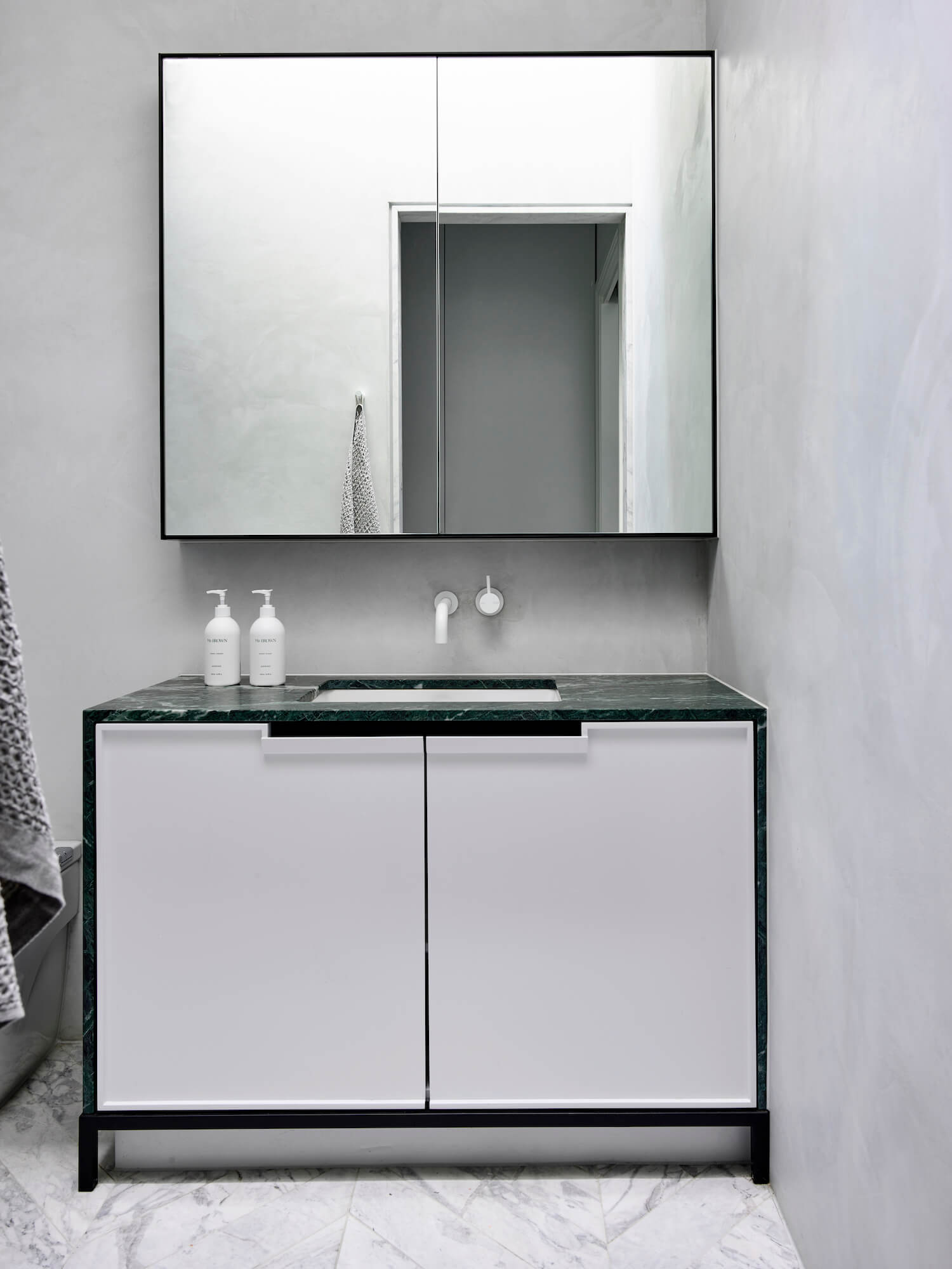 Snyggt badrum med tadelakt, grön marmor som detalj och vit marmor i chevron på golvet.