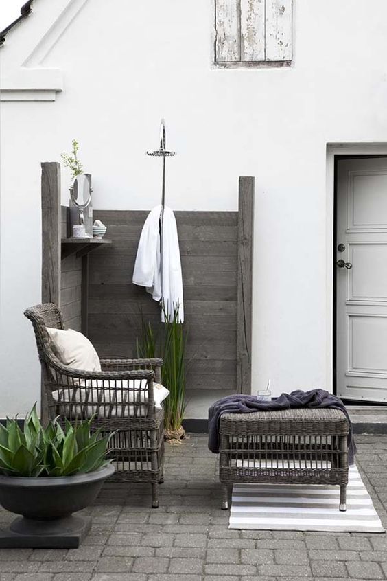 Badrumsinspiration för sommardusch - Stilren utedusch i grått trä med loungedel i rotting till vackert vitkalkat hus.
