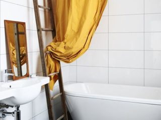 Badrumsinspiration - Duschring med gult duschdraperi ovanför ovalt badkar i enkelt badrum med vitt kakel och svart klinker.