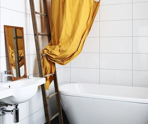 Badrumsinspiration - Duschring med gult duschdraperi ovanför ovalt badkar i enkelt badrum med vitt kakel och svart klinker.