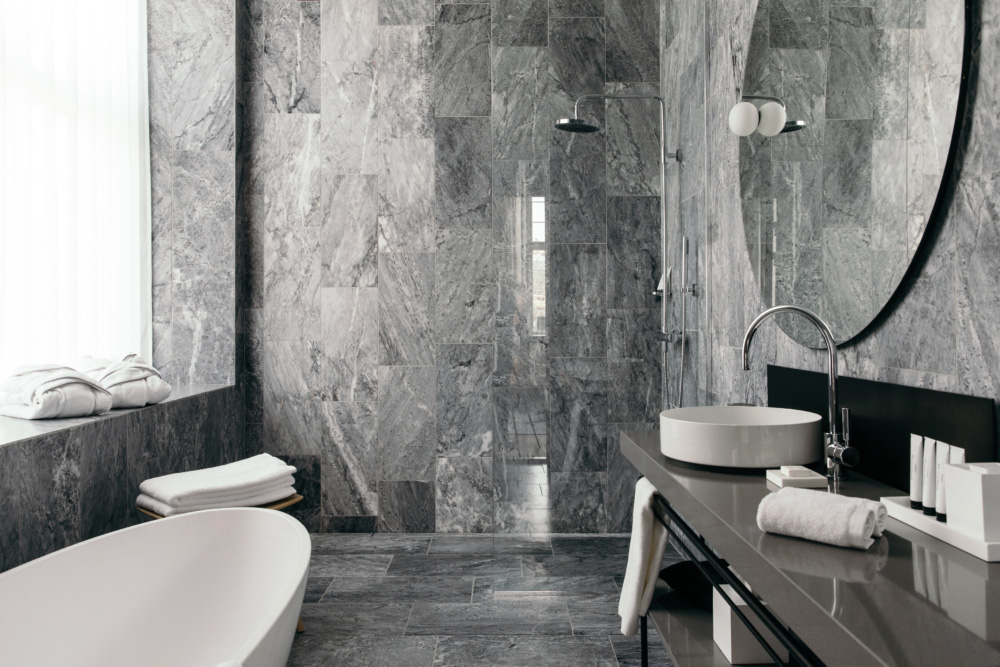 Badrumsinspiration - Grå marmor, äggformat badkar och rund spegel i badrum på Nobis Hotel Copenhagen ritat av Gert Wingårdh