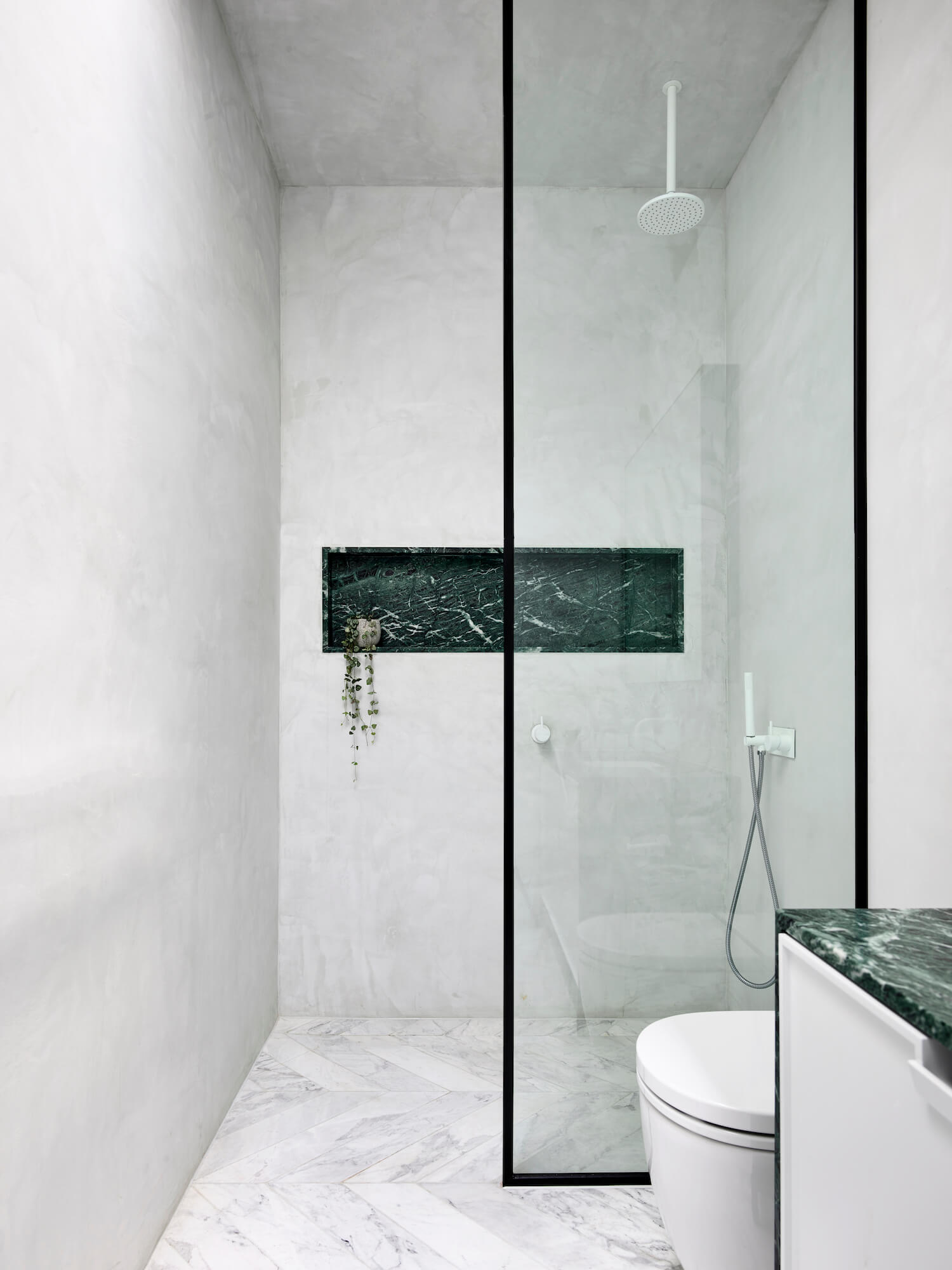Badrumsinspiration - Snyggt badrum med tadelakt, grön marmor som detalj och vit marmor i chevron på golvet.